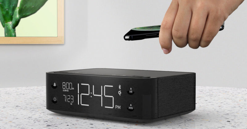 Person placing a cell phone on the alarm clock for wireless charging.